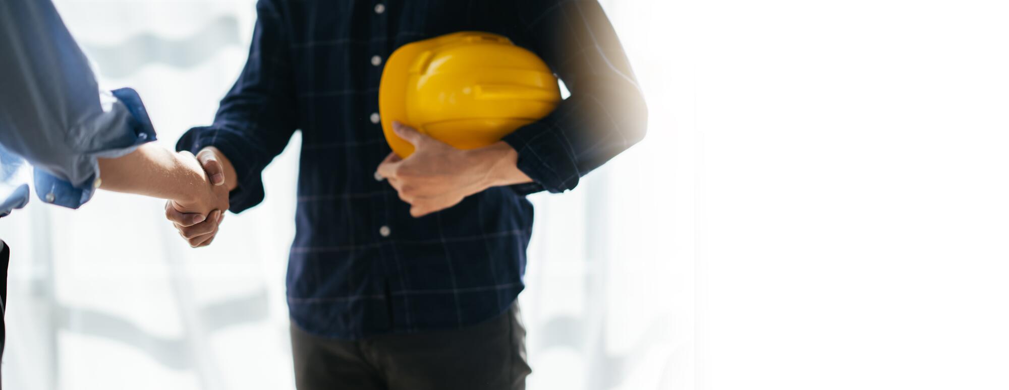 Poignée de main entre un client et un entrepreneur tenant un casque de chantier